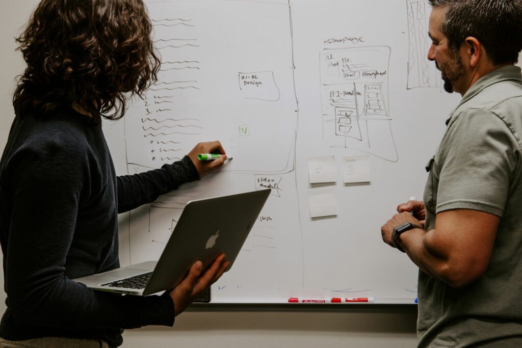 Two people using a whiteboard to design with laptop