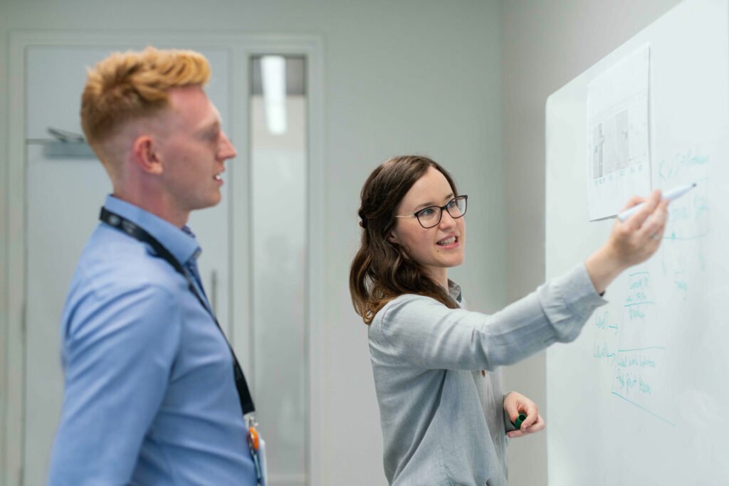 Two people in a boardroom pointing to a smartboard