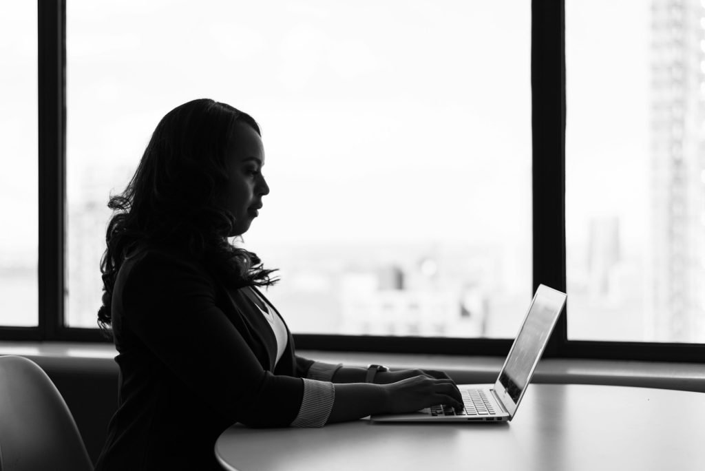black and white image of woman next to a window on a laptop