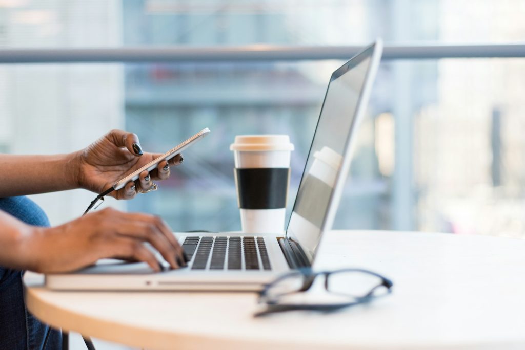 Pair of hands using a phone and laptop