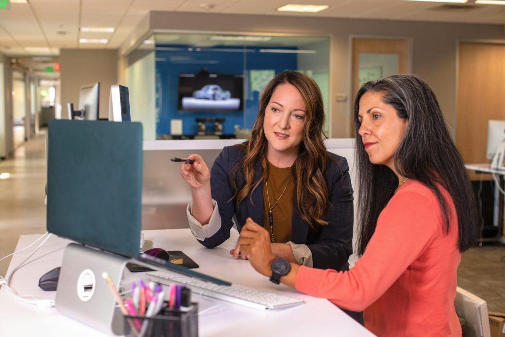 Two women sat at a desk looking at a laptop screen
