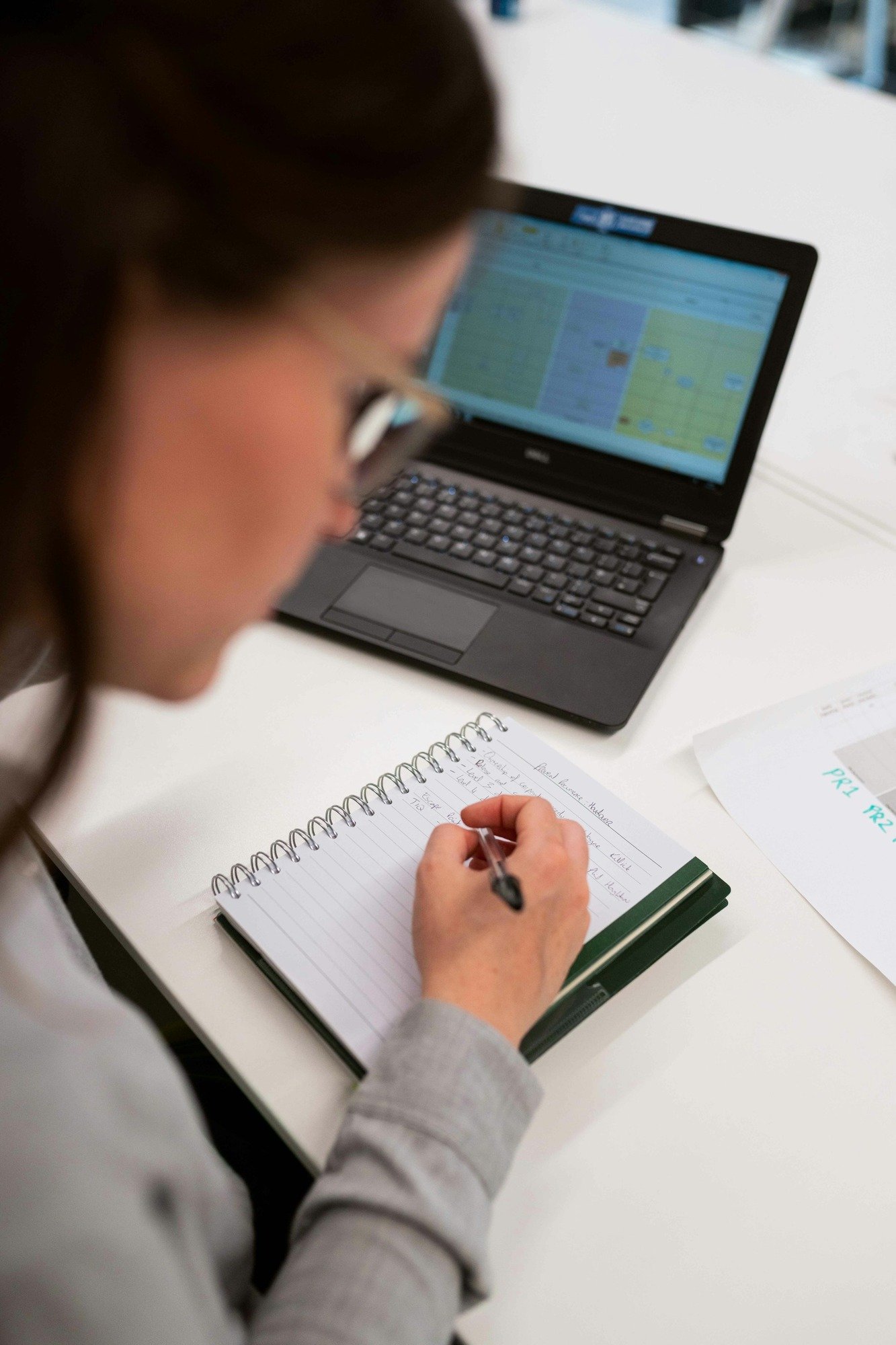 woman writing in a notepad and working on a laptop