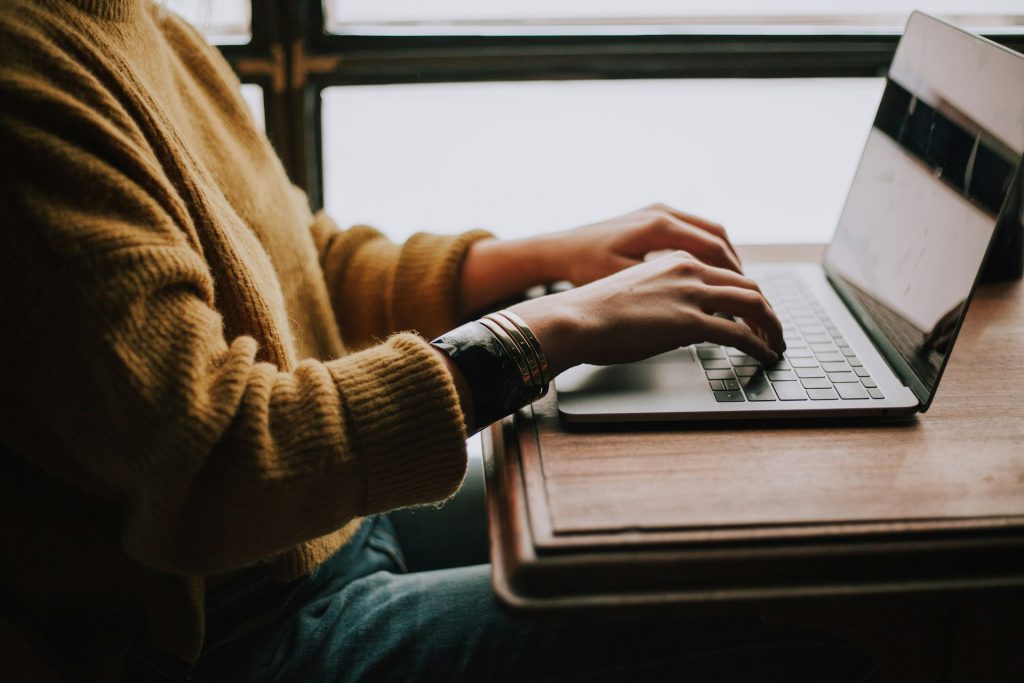 person in yellow jumper typing on a laptop